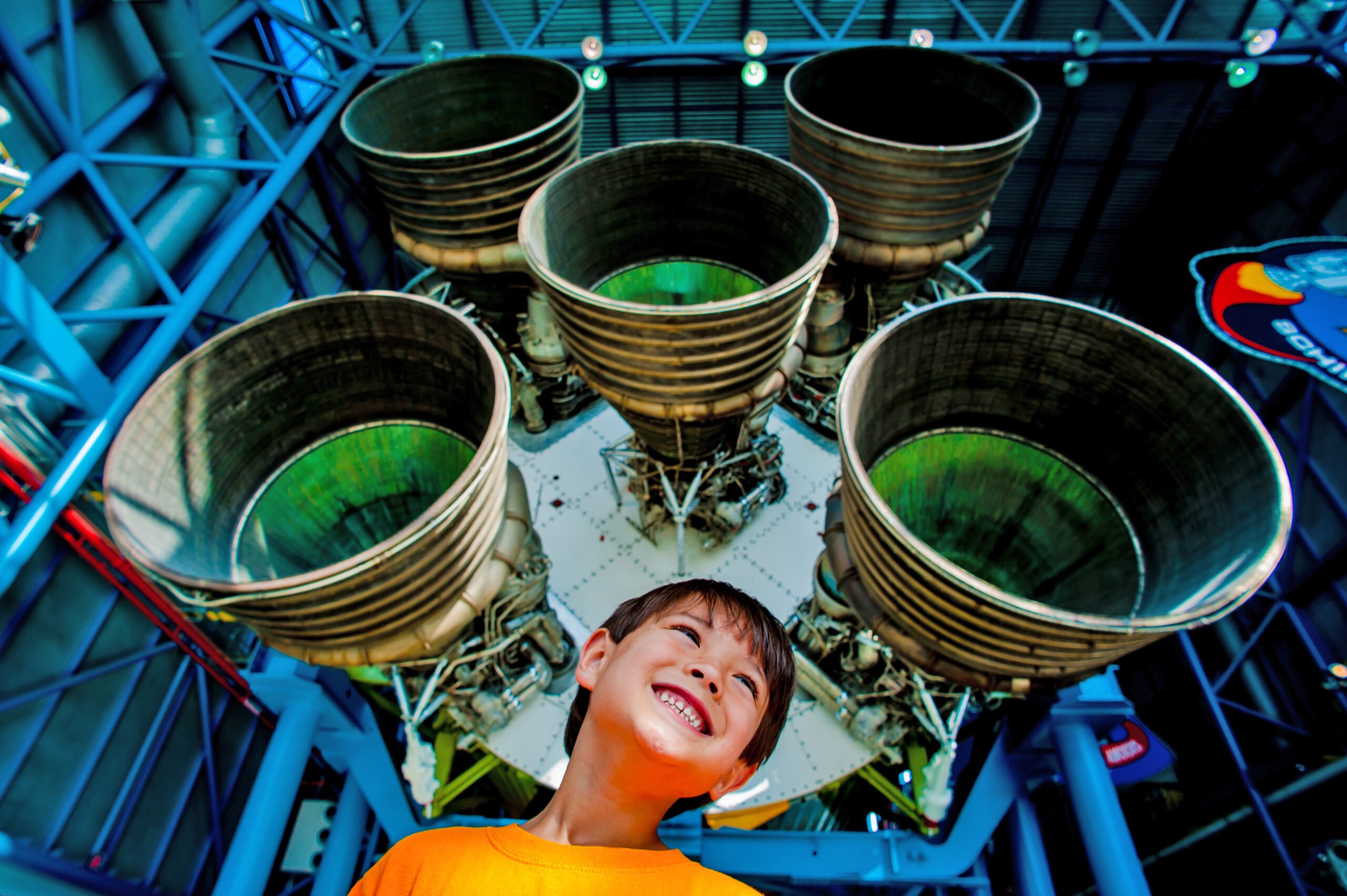 A kid smiling and having fun underneath the engine of a Saturn V rocket at Kennedy Space Center Visitor Complex in Titusville, FL