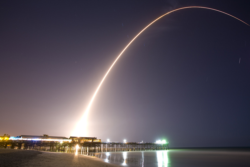 a white streak of light from a launch goes over the beach at night