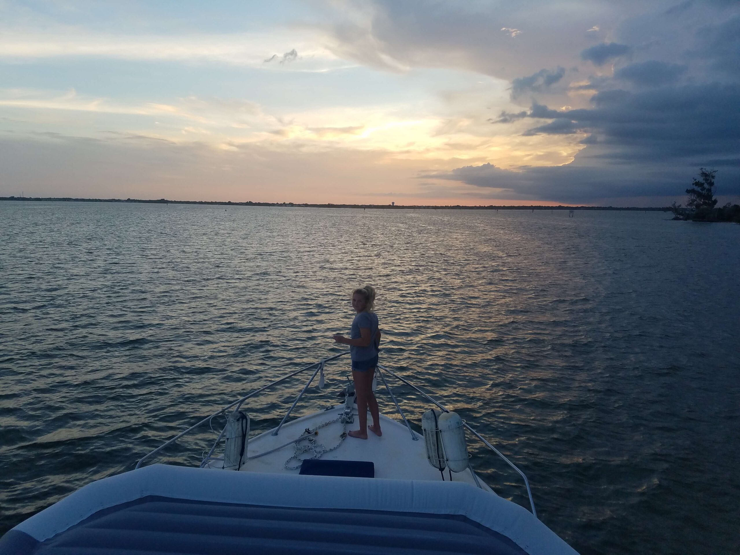 A young girl stands at the front of the boat at sunset