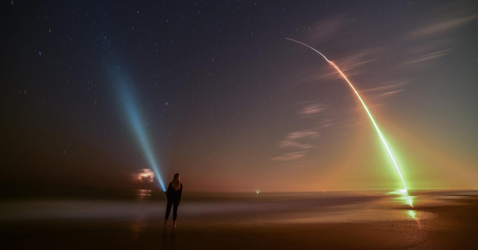 A person stands on the beach and watches a night launch