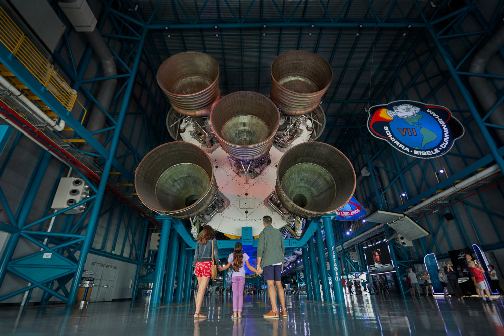 A Family takes in the scale of a Saturn V Rocket from the tail end