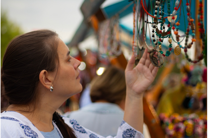 Young adult white brunette woman chooses jewelry, beads, handmade accessories for gift at street christmas fair, Tbilisoba city festival, autumn holiday, New year market. Concept of jewelry, tourism